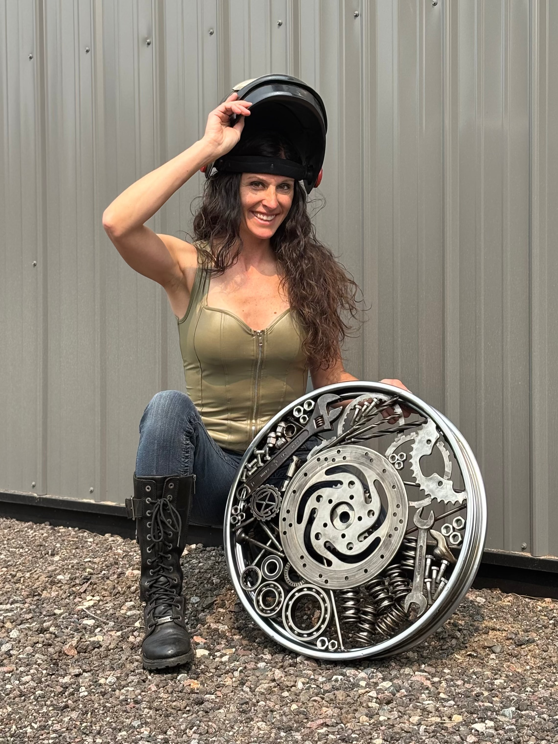 Woman holding a black helmet and a decorative metal disc against a gray wall.